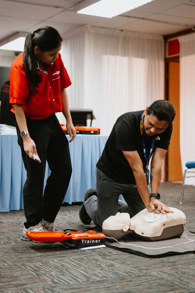 A participant practising CPR on a manikin connected to an AED trainer