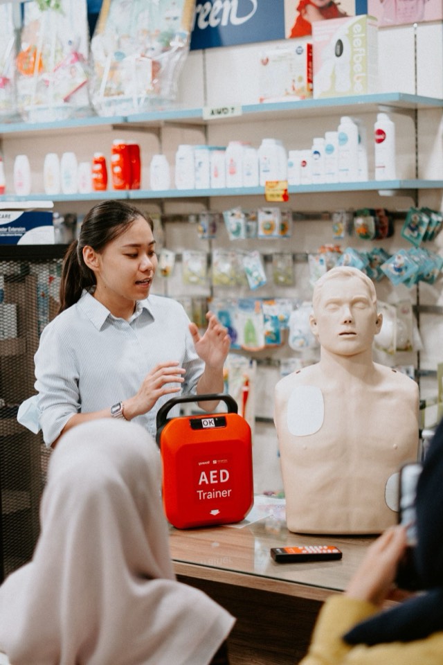 A MediShield trainer demonstrating an AED trainer and pad placement in a pharmacy